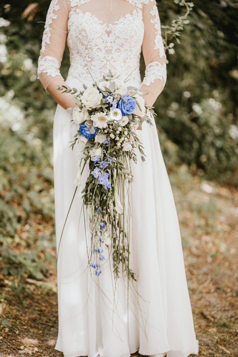 Une mariée en robe blanche tenant un bouquet conçu par un fleuriste mariage landais dans les bois.
