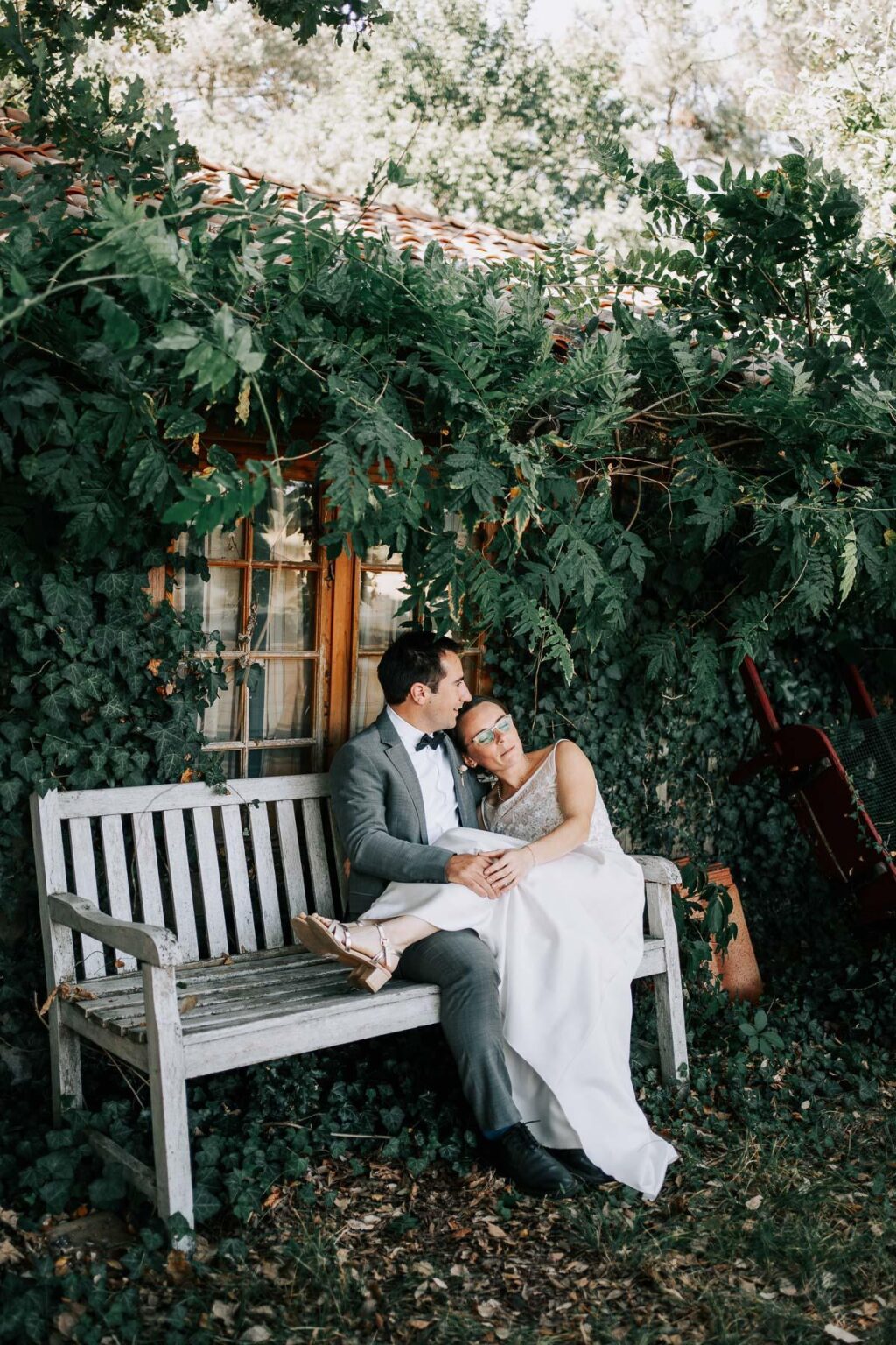 Une mariée et un marié assis sur un banc dans un jardin.