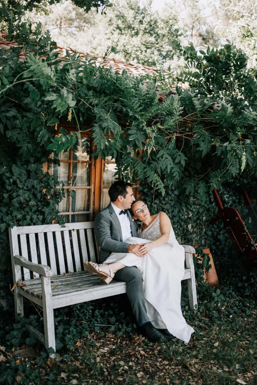 Une mariée et un marié assis sur un banc dans un jardin.