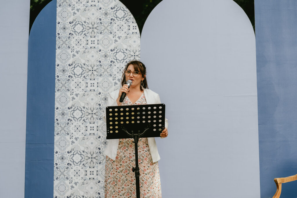 Une femme célébrant un mariage dans les Landes s'exprimant dans un micro devant un mur bleu.