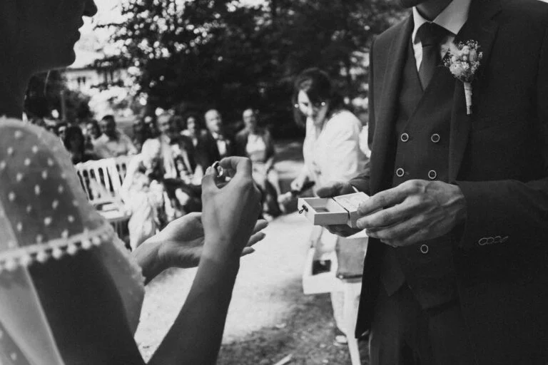 Photo en noir et blanc des mariés s'offrant un cadeau de mariage, avec en arrière-plan le célébrant landais.