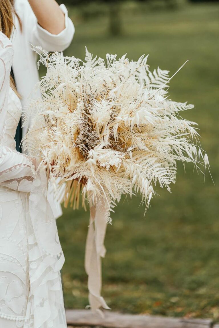 Une mariée en robe blanche tenant un bouquet d'herbes séchées créé par un fleuriste mariage landais.