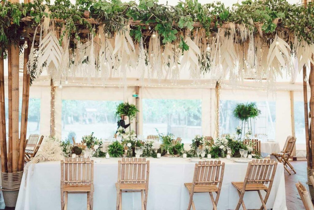 Une réception de mariage dressée sous une tente avec de la verdure suspendue au plafond, conçue par un fleuriste mariage Landais.