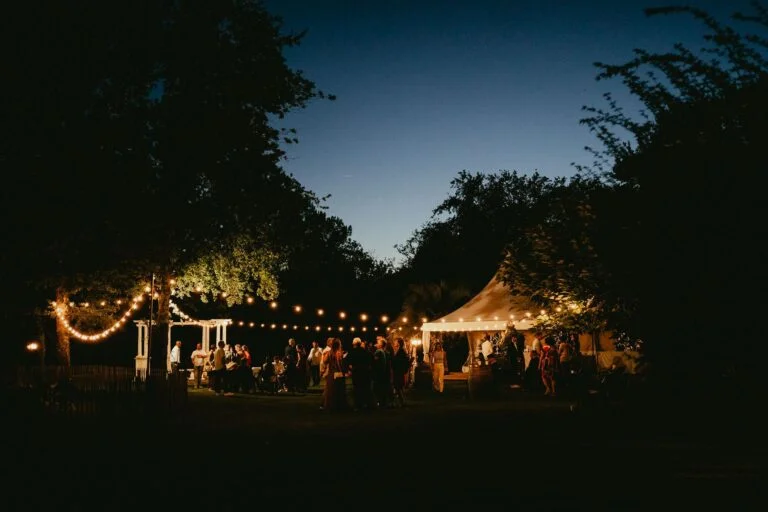 Une réception de mariage en plein air le soir avec des guirlandes lumineuses.