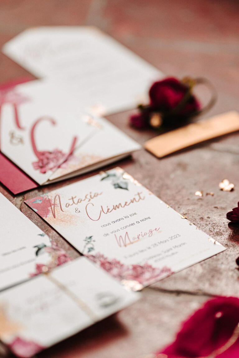 Une "papeterie mariage Landes" rouge et or posée sur une table.