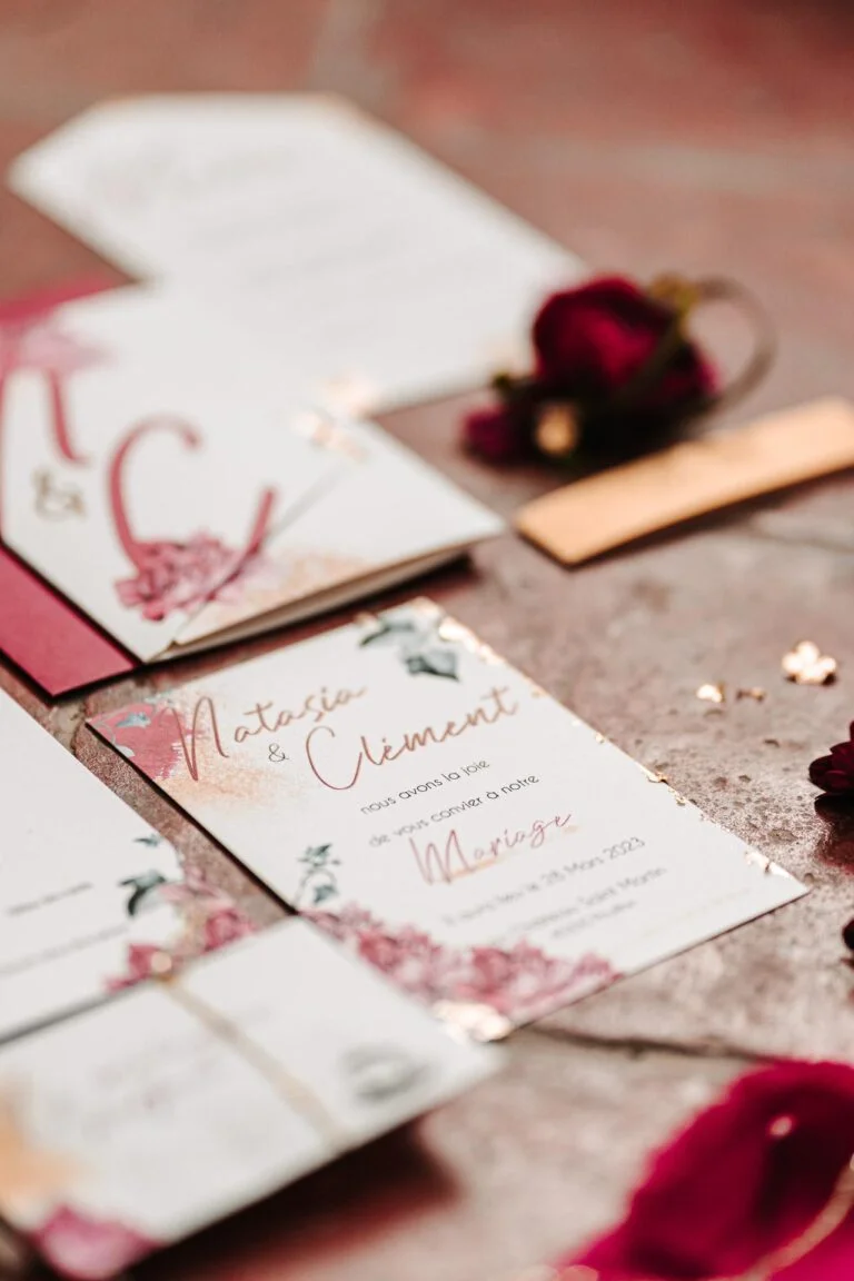 Une "papeterie mariage Landes" rouge et or posée sur une table.