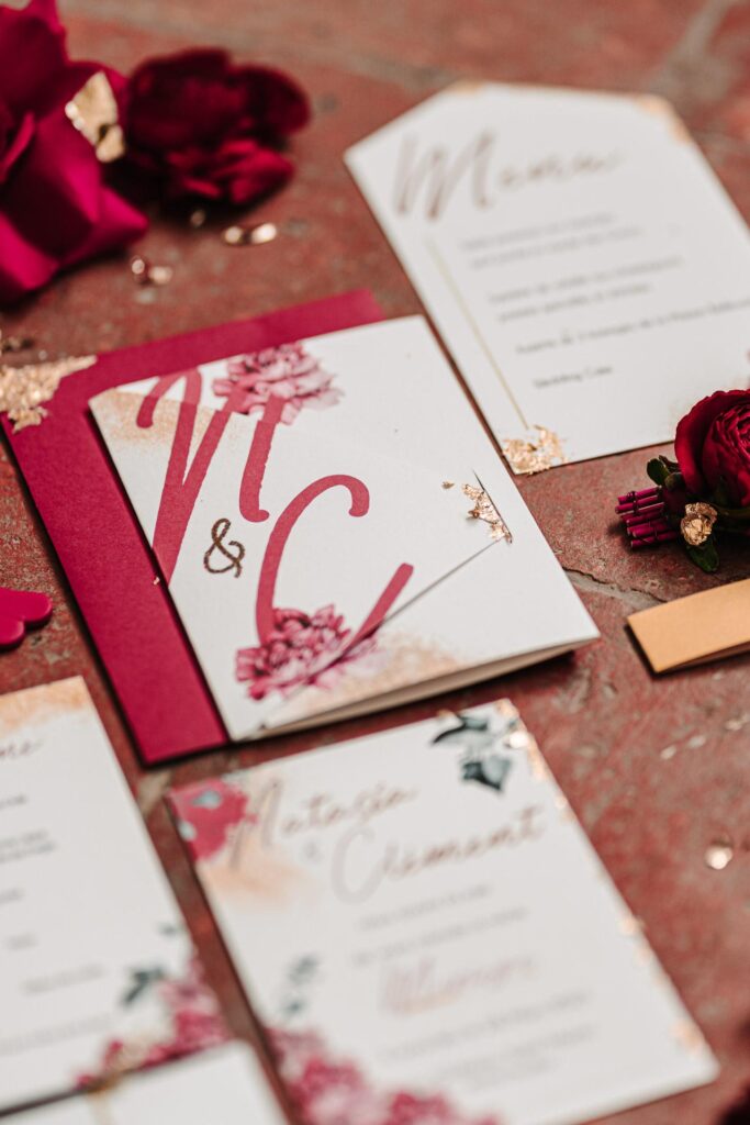 Une invitation à un mariage landais en papeterie avec des roses rouges et des lettres dorées.