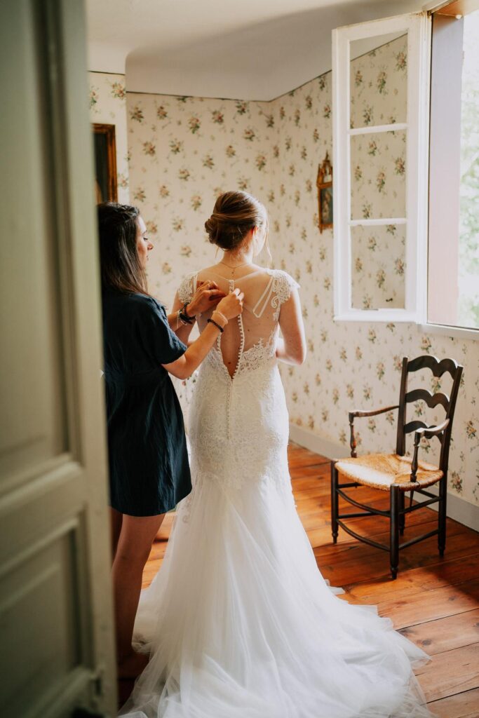 Une mariée se prépare dans une chambre avec fenêtre, vêtue de sa magnifique robe de mariage landaise.