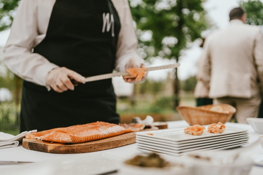 Un traiteur prépare du saumon sur une table en plein air pour un mariage dans les Landes.