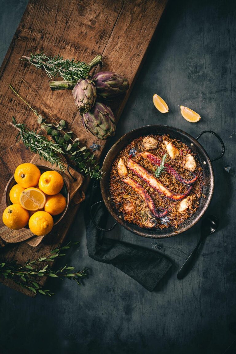 Une poêle avec du poisson, des légumes et de l'arroz sur une table en bois.