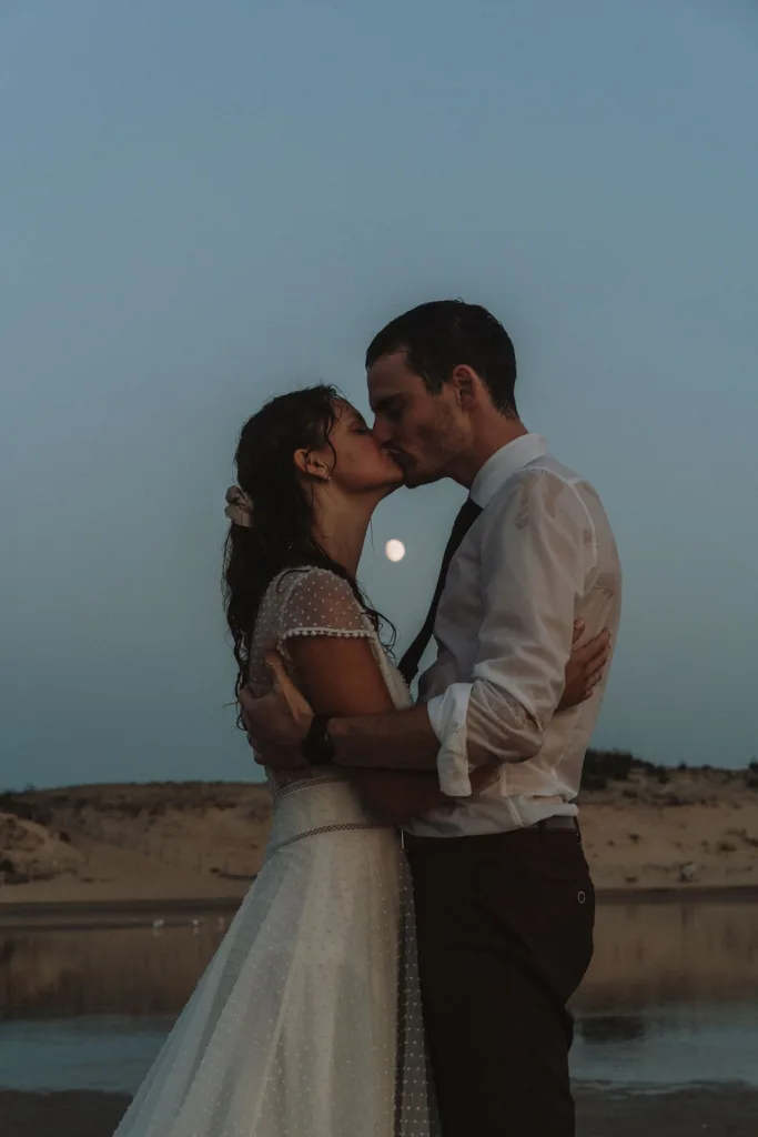 des mariés s'embrassant avec la lune derrière eux
