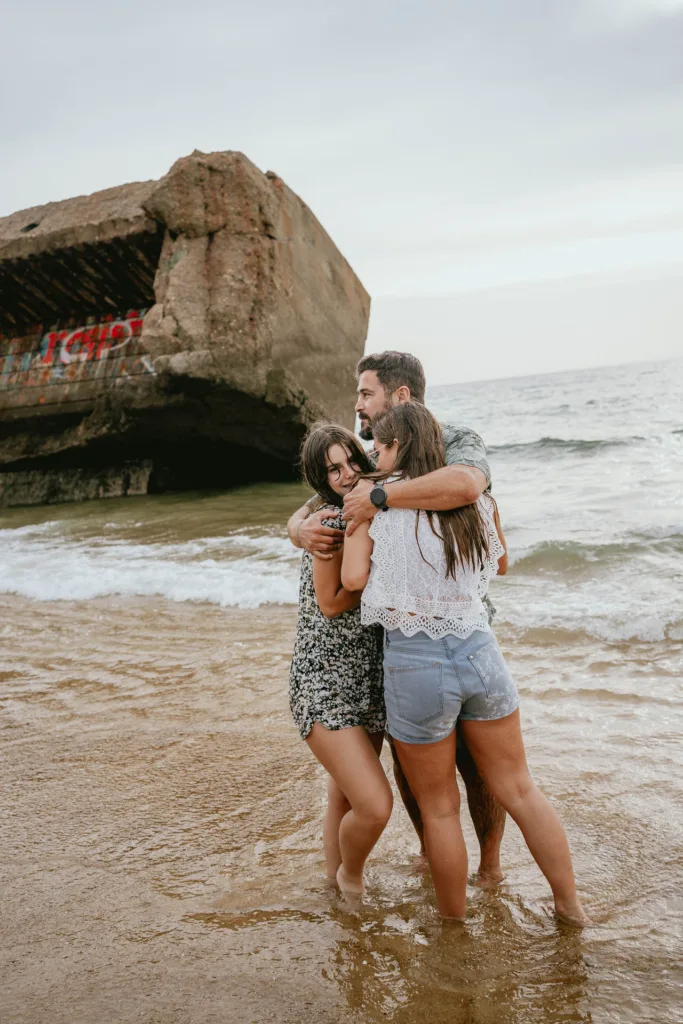 Trois personnes s'enlaçant dans l'océan près d'une formation rocheuse pour une séance photo en famille.