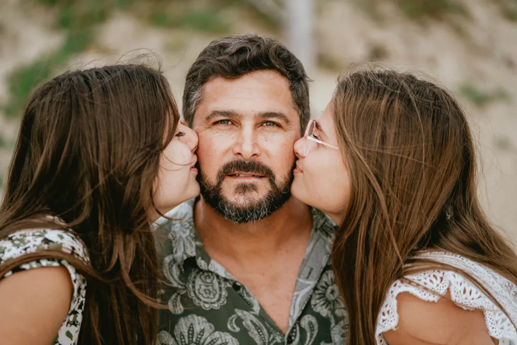 Un homme embrassant ses filles sur la plage lors d’une séance photo de famille.