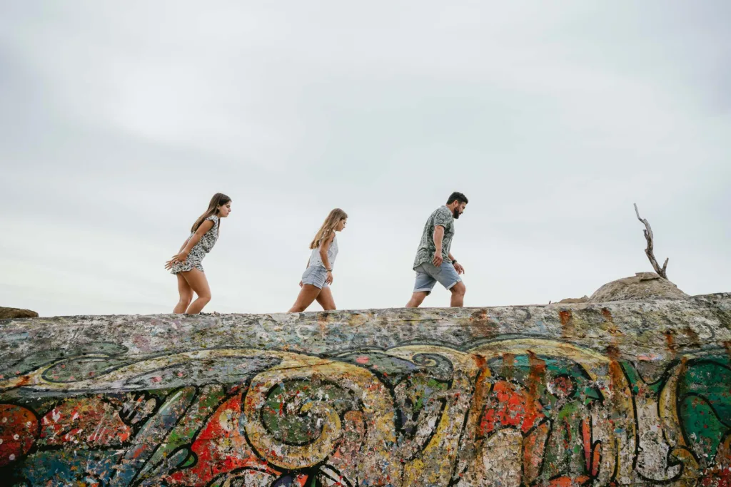 Trois jeunes gens marchant sur un rocher couvert de graffitis au bord de l'océan.