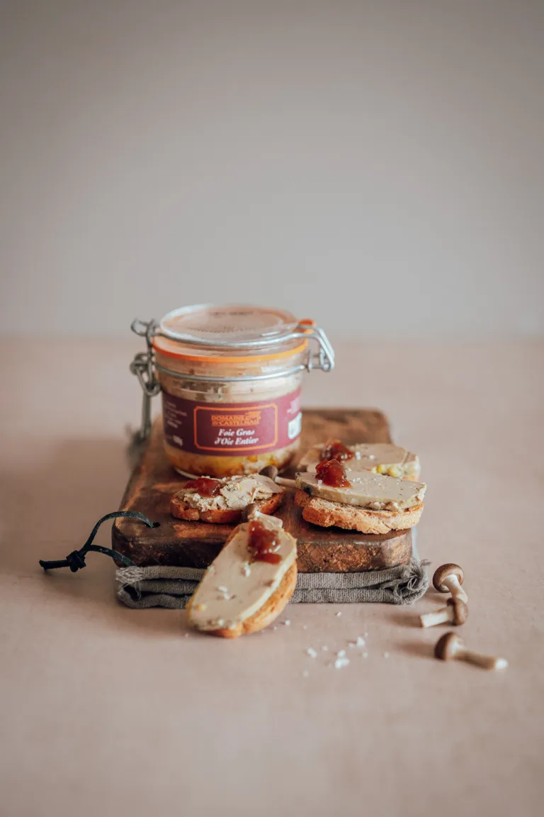 Un pot de foie gras est posé sur une planche en bois avec deux tartines de pain, pour un shooting culinaire.
