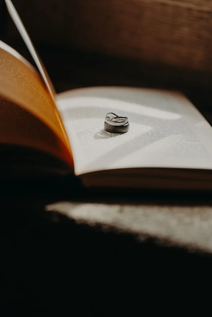 Une bague en argent posée sur les pages ouvertes d'un livre, projetant sur le texte une ombre en forme de cœur, rappelant l'amour trouvé dans un mariage en Italie.