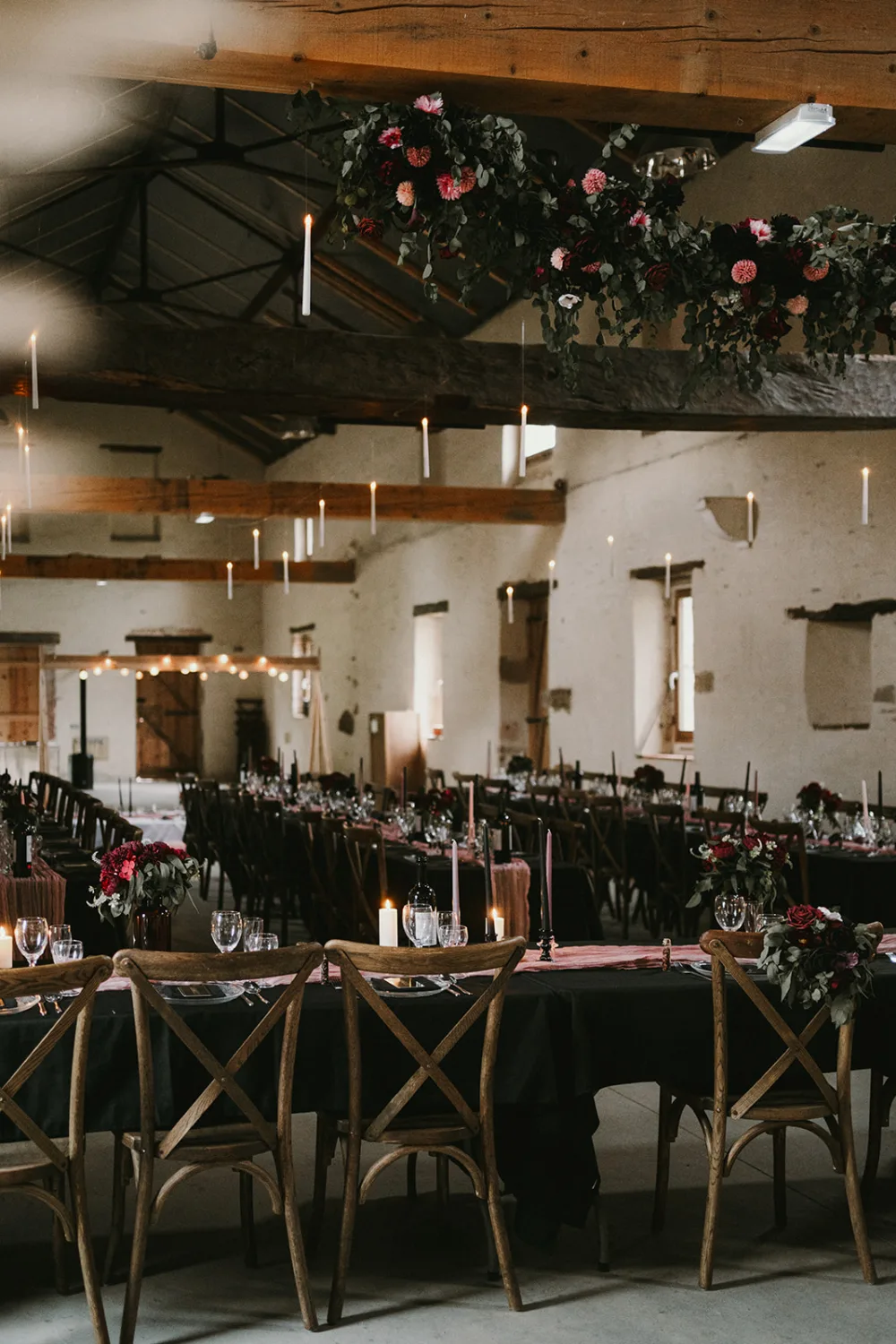 Un photographe famille Landes talentueux pourrait immortaliser la magie d'une réception de mariage rustique dans une salle aux poutres en bois, où de longues tables ornées de bougies, fleurs et verres à vin créent une ambiance chaleureuse ; des arrangements floraux élégants suspendus au plafond accentuant l'atmosphère enchanteresse idéale pour des souvenirs mémorables de mariage ou de famille dans les Landes.