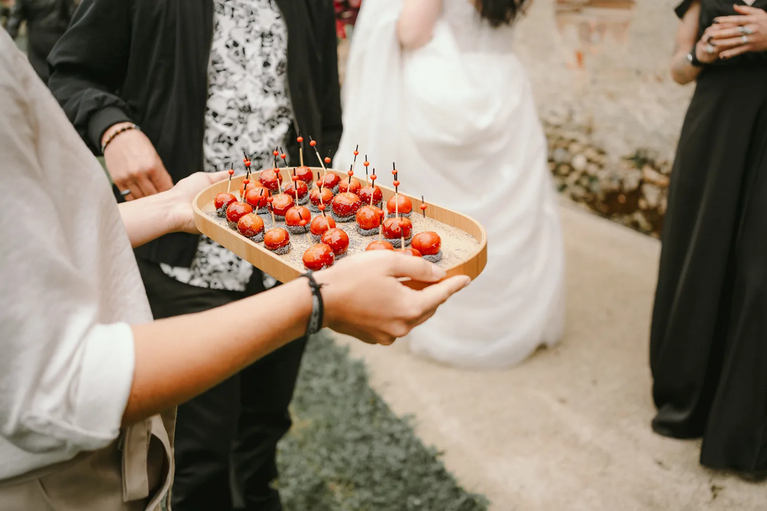 Lors d'un élégant événement dans les Landes, un serveur en tenue formelle présente un plateau de savoureuses brochettes rouges, tandis que les invités en costumes et robes de soirée ajoutent une touche de sophistication à cette scène capturée par un photographe spécialisé en mariage et famille. dans les Landes.