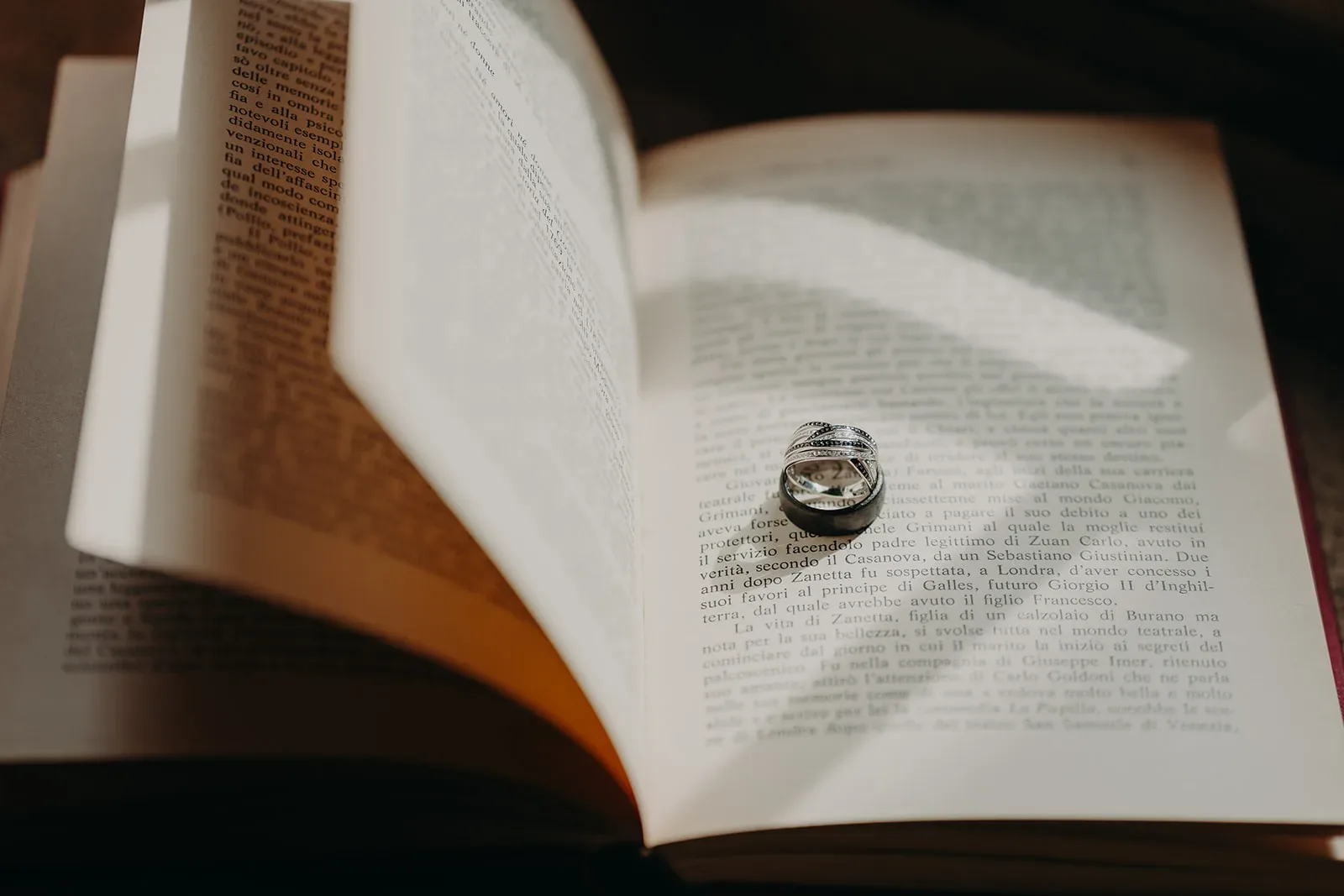 Un anneau en argent repose délicatement sur un livre ouvert, projetant une ombre en forme de cœur sur les pages, immortalisé à la perfection, rappelant les moments précieux et intimes que seul un photographe de mariage ou de famille dans les Landes sait capturer avec tant d'émotion. et de précision.