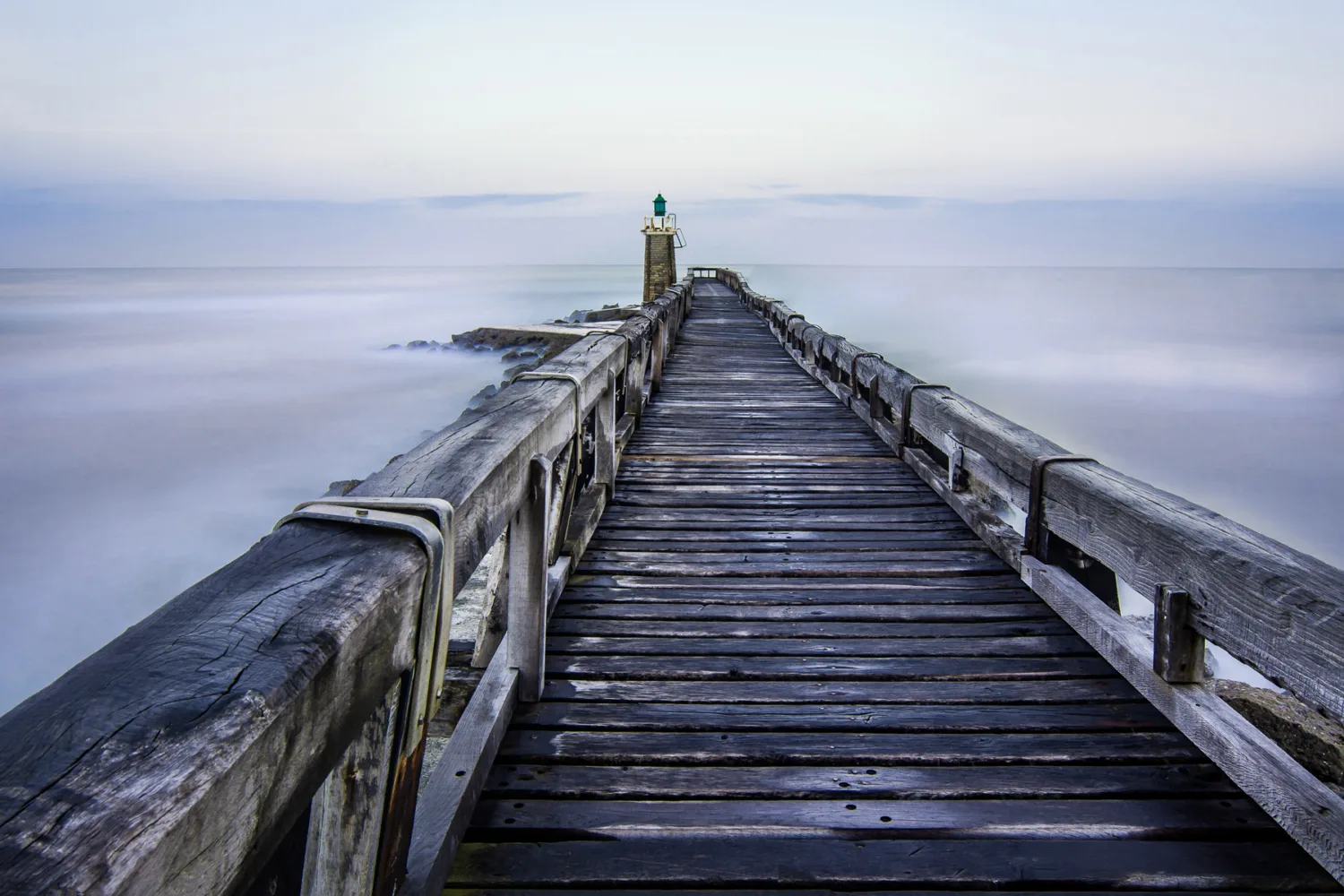 Voici une description optimisée pour le référencement : Un ponton en bois s'étend dans la mer calme, conduisant à une petite structure dotée d'une lumière verte à son extrémité, rappelant les vacances idylliques à Porto; le ciel est nuageux et les vagues caressent doucement les côtés du ponton, créant une ambiance parfaite pour des séances photo uniques de mariage ou de famille dans les Landes.