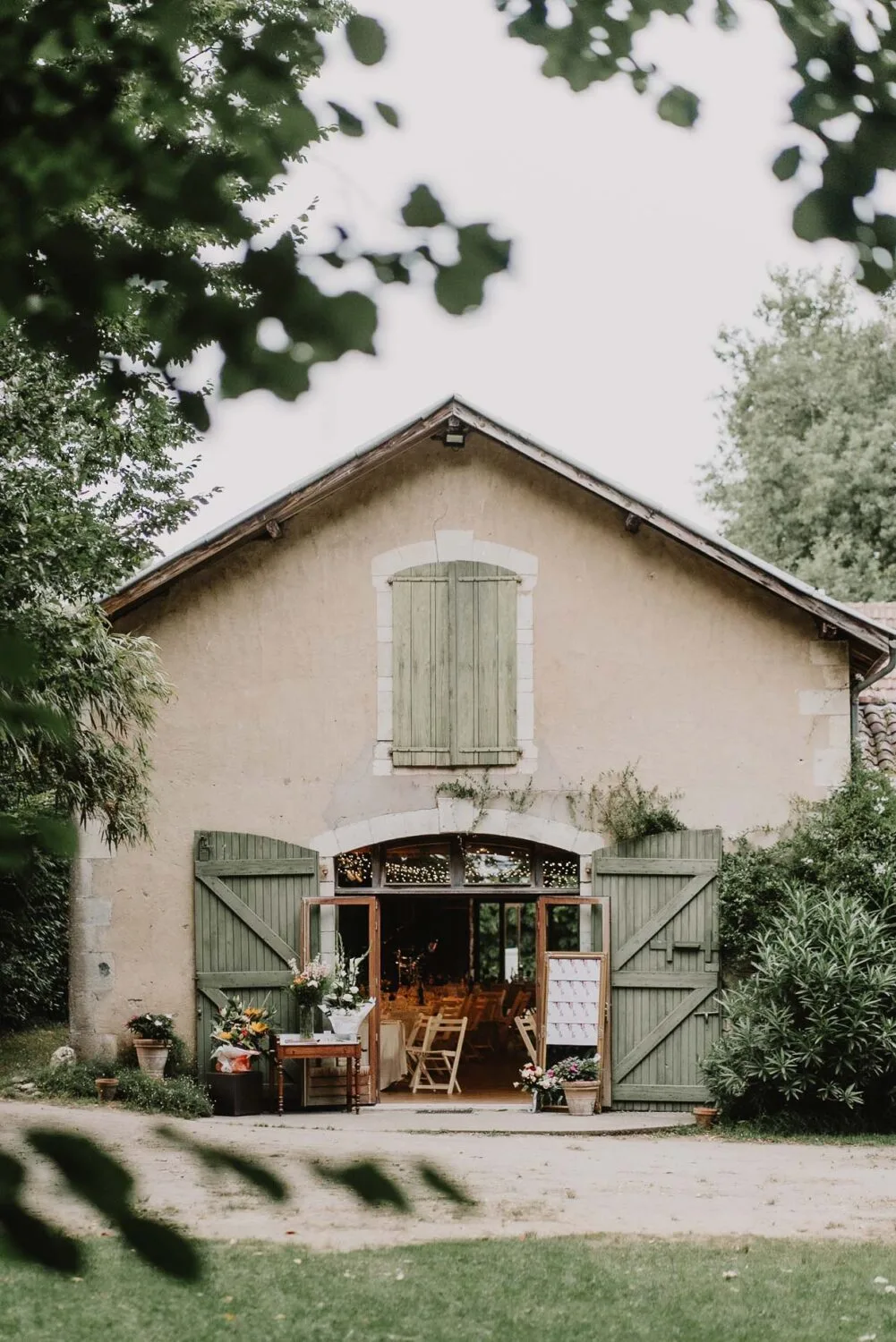 Cette image captivante d'une journée ensoleillée dans les Landes présente un bâtiment rustique aux volets verts et portes ouvertes, entouré de verdure luxuriante, offrant une scène pittoresque idéale pour un photographe famille Soustons; à l'intérieur, une table et des chaises attendant pour accueillir des moments inoubliables et créer des souvenirs précieux lors d'une séance photo mariage ou famille dans ce cadre enchanteur.