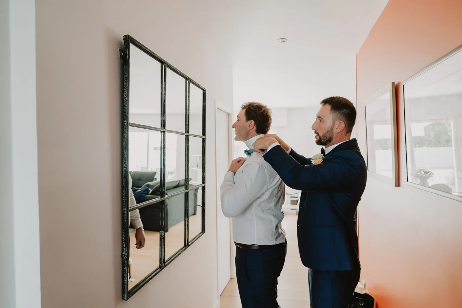 Dans la douce lueur d'un couloir, évoquant une scène authentique digne d'un photographe de mariage ou famille dans les Landes, notamment à Soustons, deux hommes se respectent proches, l'un ajustant avec attention le nœud papillon de l'autre devant un miroir ; une image qui capture magnifiquement leur lien intime et complice, idéale pour illustrer des moments précieux chéris par des photographes spécialisés en portraits familiaux et en mariages dans cette région pittoresque.