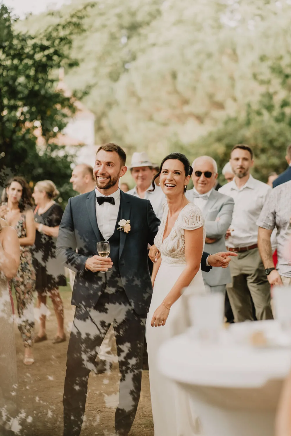 Lors d'une magnifique réception en plein air capturée par le talentueux photographe famille Soustons spécialisé dans les mariages dans les Landes, une mariée éblouissante et un marié radieux échangent des sourires complices tandis que leurs invités partagent des moments joyeux en arrière-plan, créant une ambiance chaleureuse et inoubliable.