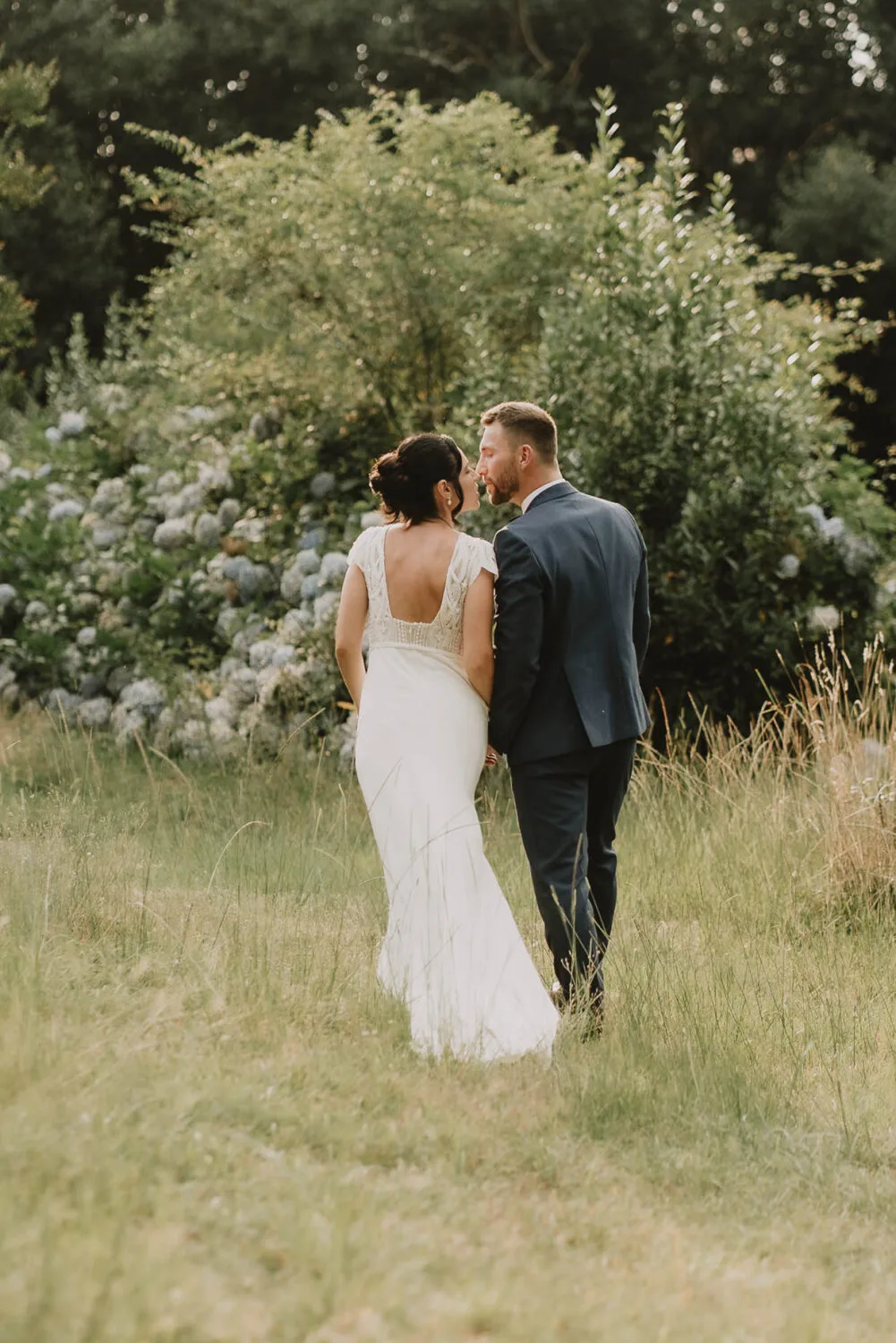 Dans cette image pittoresque optimisée pour le référencement en tant que photographe mariage et famille dans les Landes, un couple de mariés se tient tendrement dans un champ verdoyant, entouré d'une végétation luxuriante et de superbes hortensias en fleurs en arrière-plan, le tout immortalisé avec élégance par un photographe famille à Soustons.