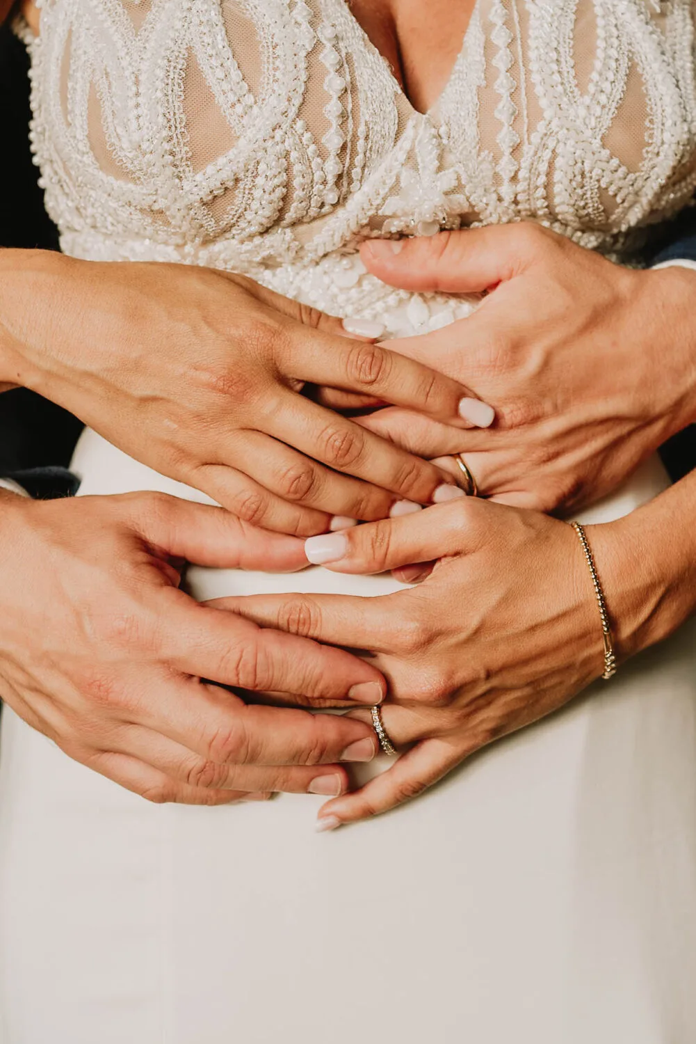 Dans cette image captivante, réalisée par un photographe de mariage et famille basée à Soustons, les mains entrelacées du couple mettent en valeur leurs alliances scintillantes, tandis que la mariée affiche une élégante robe en dentelle et le marié arbore un costume sombre, illustrant parfaitement l 'art de la photographie familiale dans les magnifiques paysages des Landes.