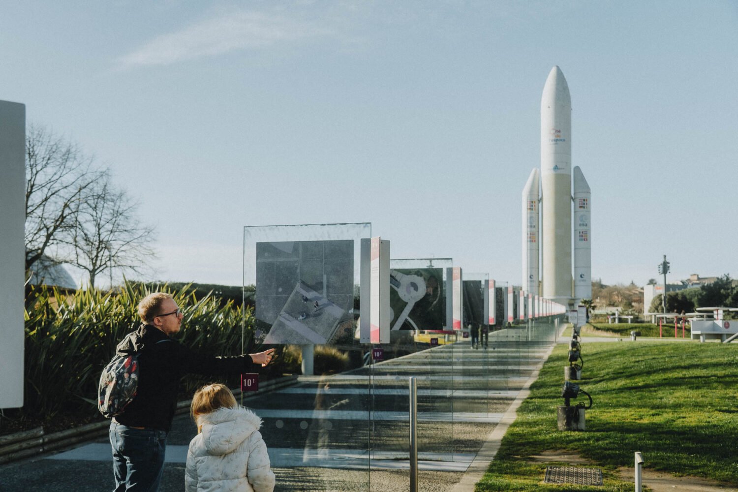 Un père et son enfant découvrent ensemble une rangée de présentoirs informatifs situés à côté d'une majestueuse fusée dans un cadre extérieur, capturant des moments inoubliables et authentiques distinctifs pour renforcer l'album "Guide 4 jours en famille à Toulouse", mettant en valeur l'essence du tourisme familial et l'esprit d'aventure que les photographes de mariage et de famille recherchent souvent dans les Landes pour créer des souvenirs émouvants.