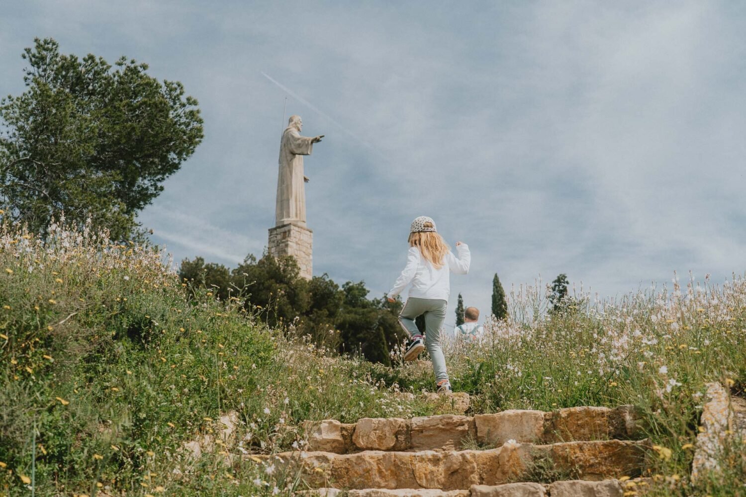 Deux enfants gravissent des marches en pierre, main dans la main, vers une statue majestueuse. Instant d’aventure en famille aux Bardenas Reales.