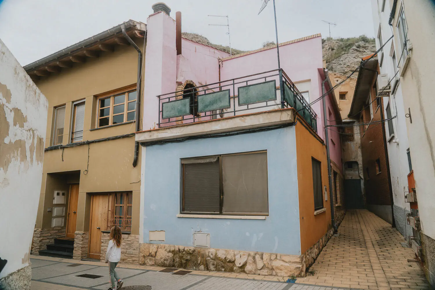 Cette photo saisit une scène authentique : une fillette passe devant une maison colorée, ambiance douce et familiale en Espagne.