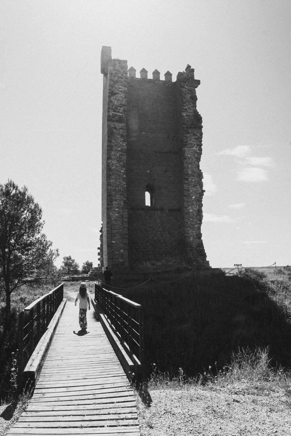 Une balade en famille sur un pont de bois, vers une tour ancienne, lumière douce et ambiance d’aventure dans l'Espagne.