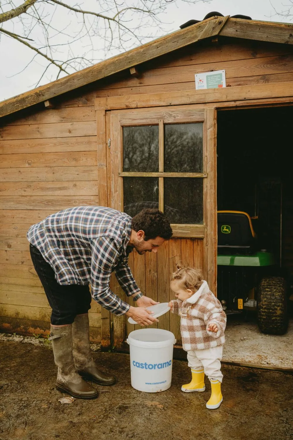Un doux moment de complicité, un adulte guide un enfant près d’un abri en bois, ambiance authentique de Dax.
