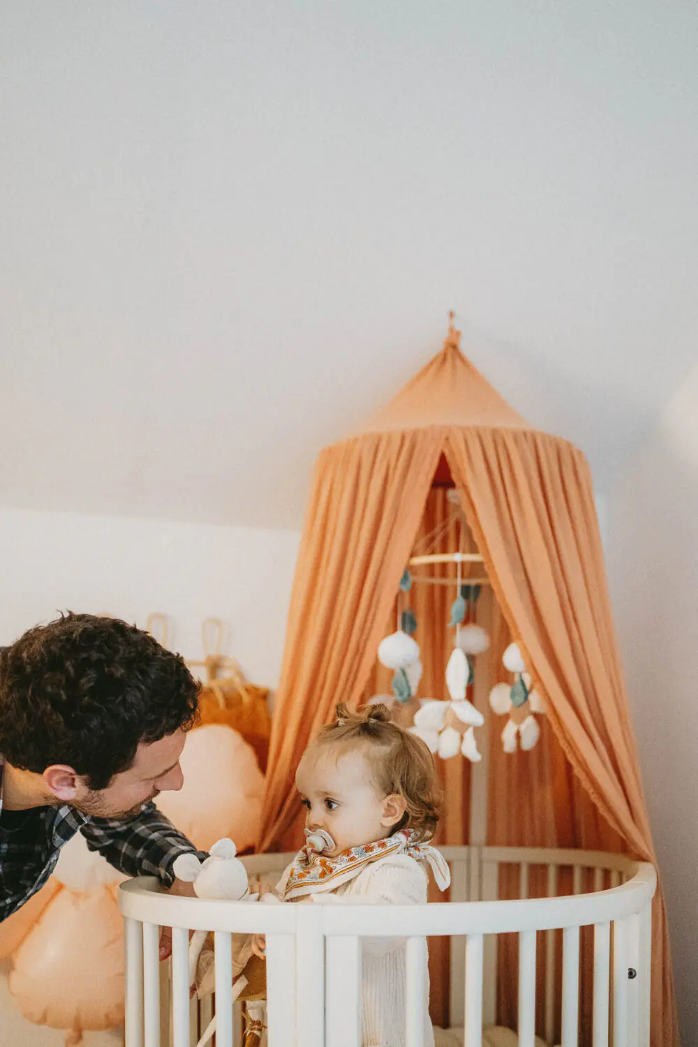 Une scène tendre de famille à Dax: un adulte partage un doux moment près du berceau, où règne une douce ambiance de mariage.