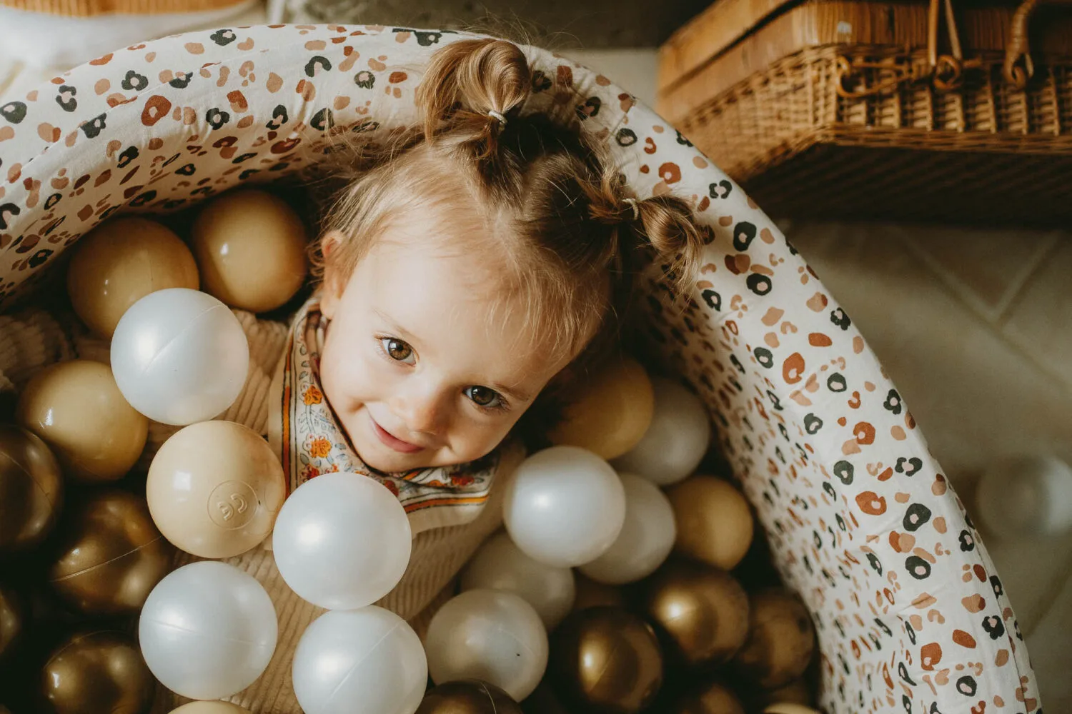 Un doux instant volé à Dax : votre petite fille rayonne, allongée parmi des balles dorées et blanches.