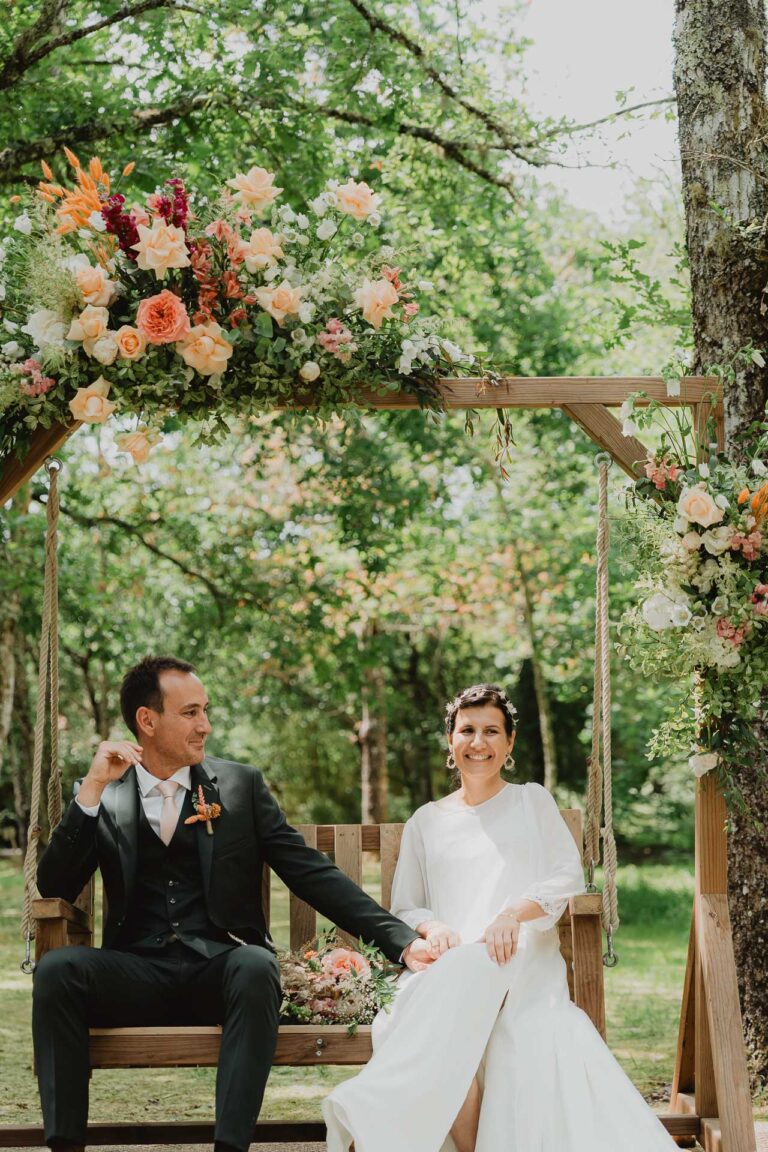 Céline et Nicolas, complices, sourient sur une balançoire fleurie au domaine de Petiosse, ambiance bohème et naturelle.