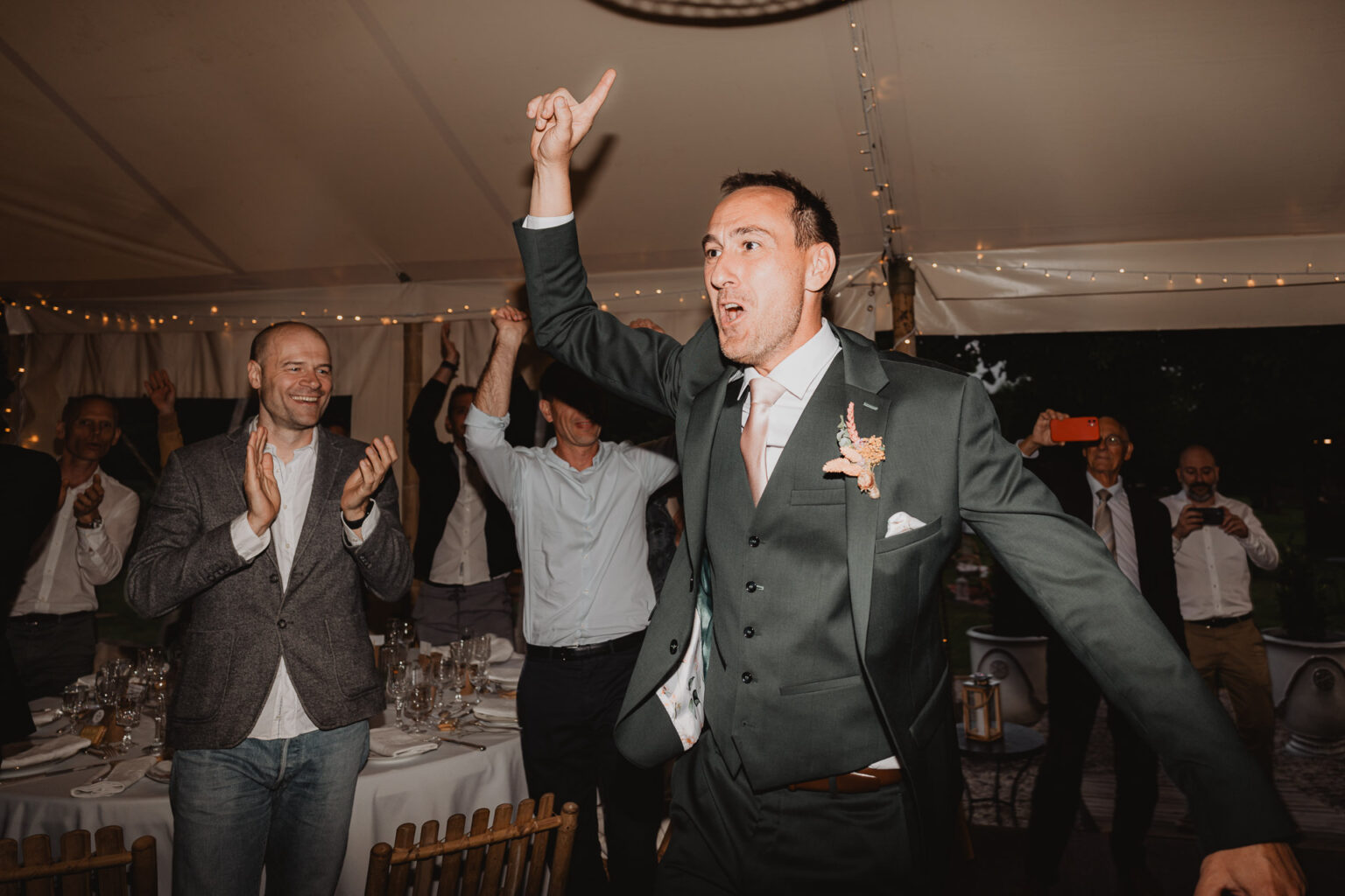 Un homme en costume entre joyeusement sous la tente au Domaine de Petiosse, entouré d'applaudissements et d'émotion festive.