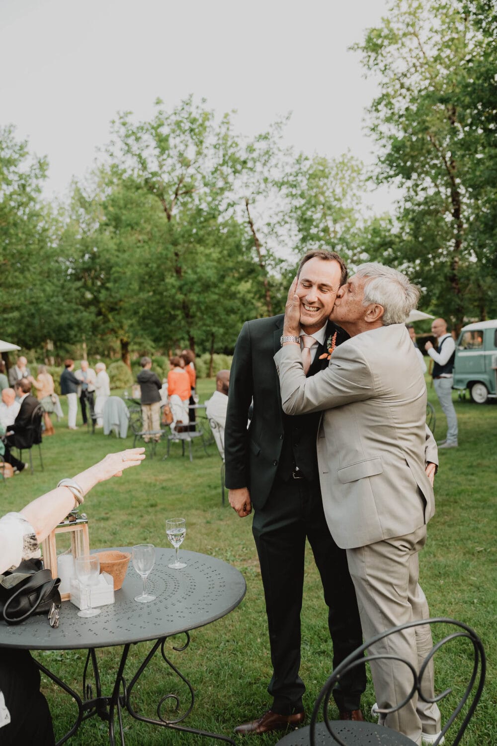 Moment complice entre un père et son fils à un mariage au domaine de Petiosse, sous le regard attendri des invités.