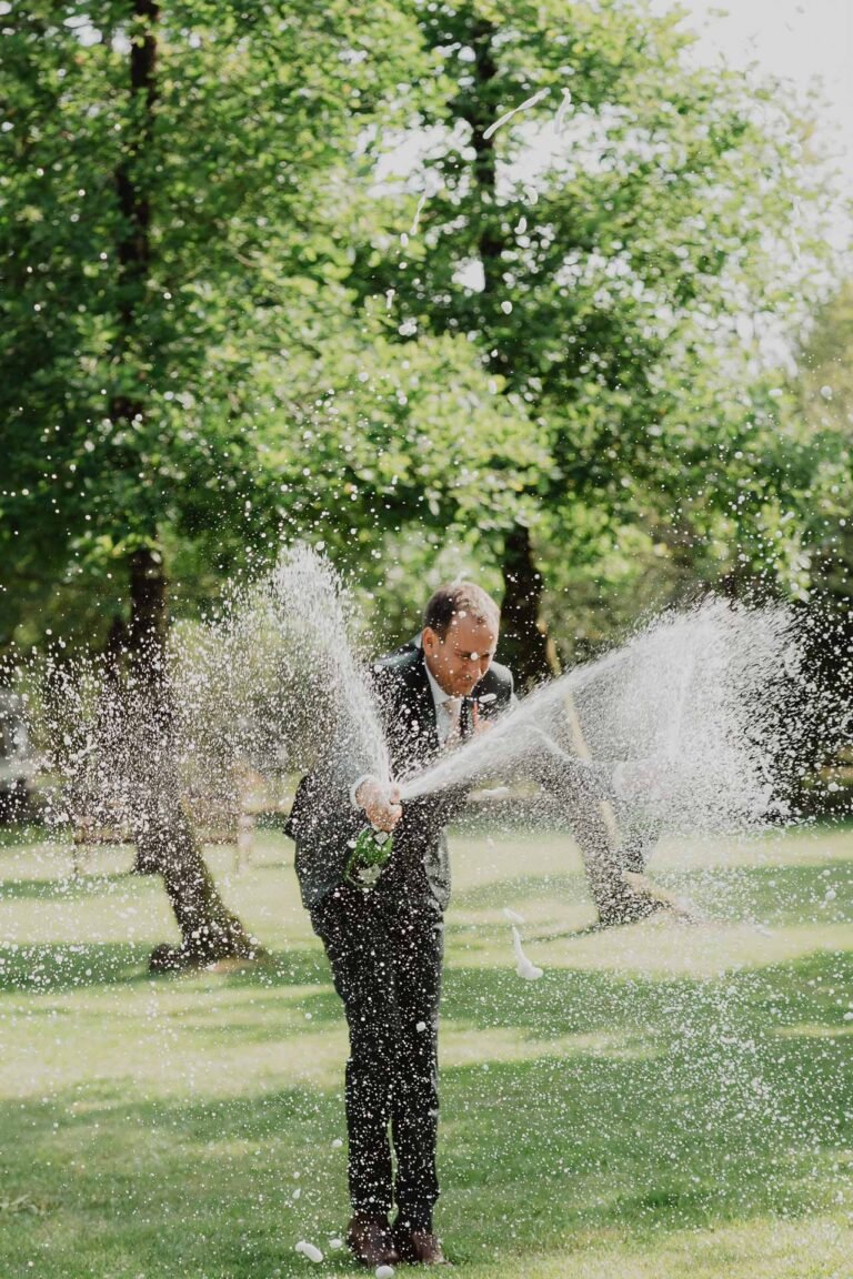 Nicolas, élégant en costume, célèbre en plein air au domaine de Petiosse, éclaboussant de joie sous les arbres landais.