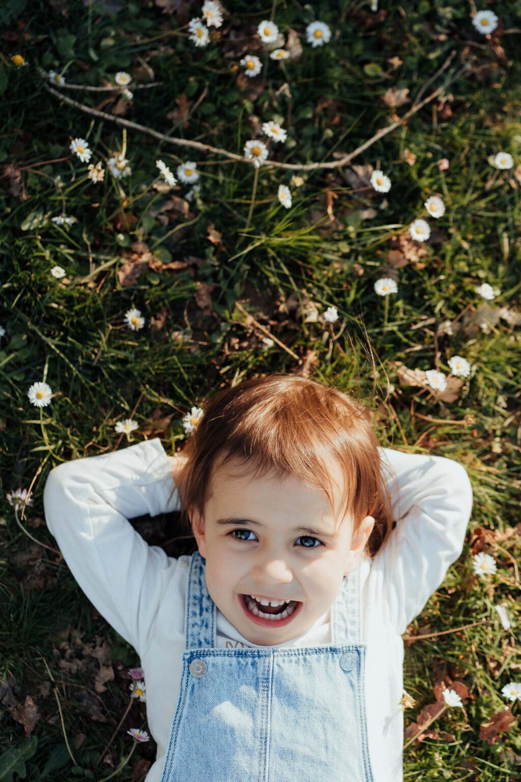 Un moment de douceur capturé dans la nature landaise : un enfant rayonnant, allongé dans l'herbe fleurie, insouciant et heureux.