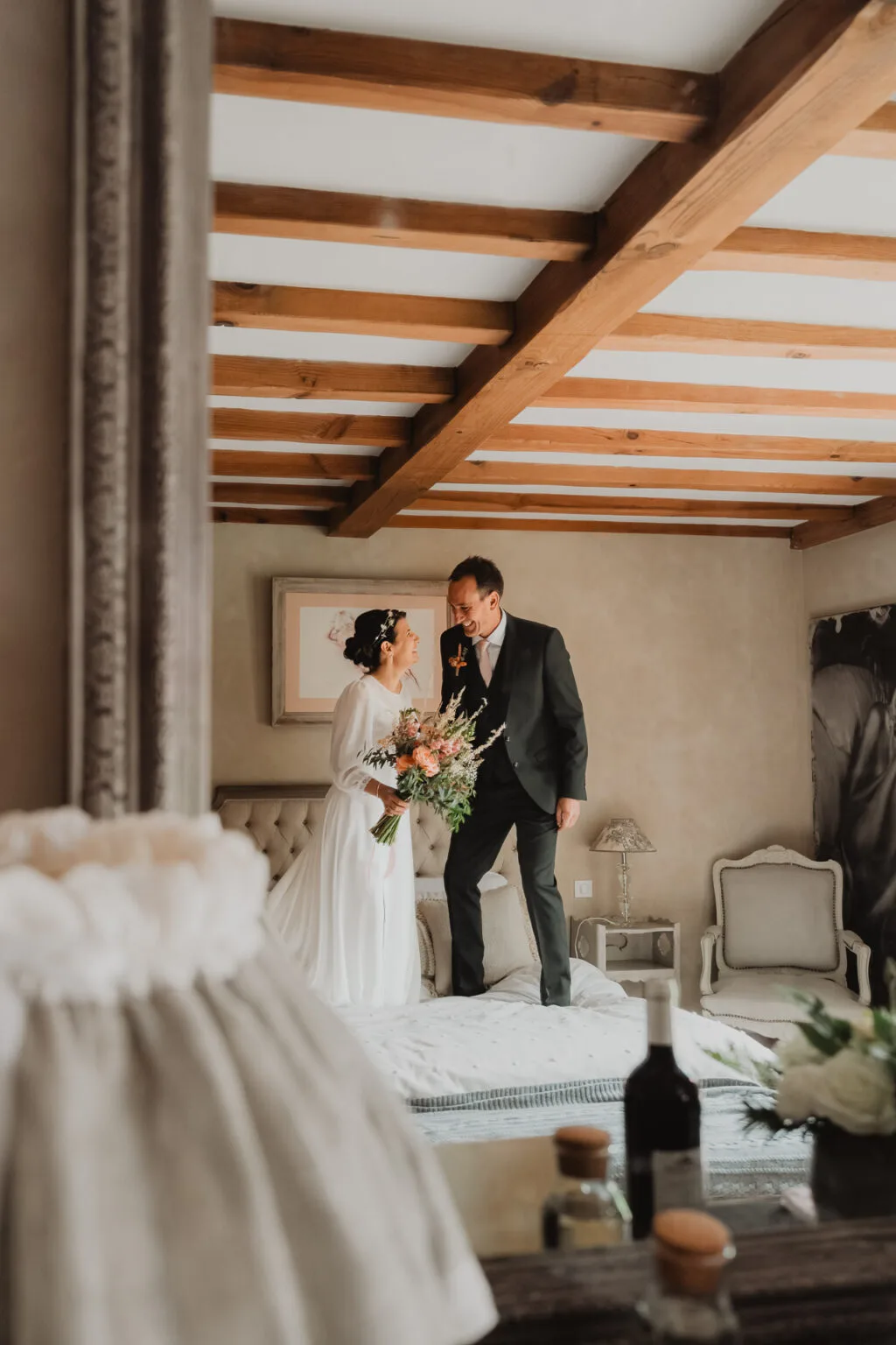 Céline et Nicolas, rayonnants, debout sur le lit au domaine de Petiosse, échangent un regard complice sous une lumière douce.