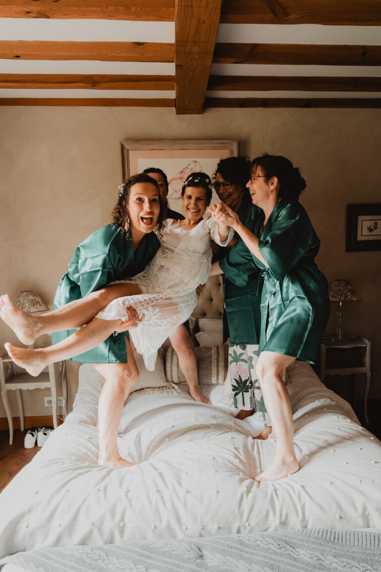 Une vraie complicité de mariage : amies en peignoirs verts rient, portent la mariée dans une chambre douce aux Landes.