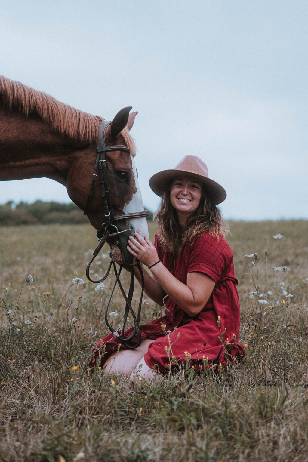 Une femme en robe rouge, sourire tendre, nourrit un cheval pendant une seance photo.