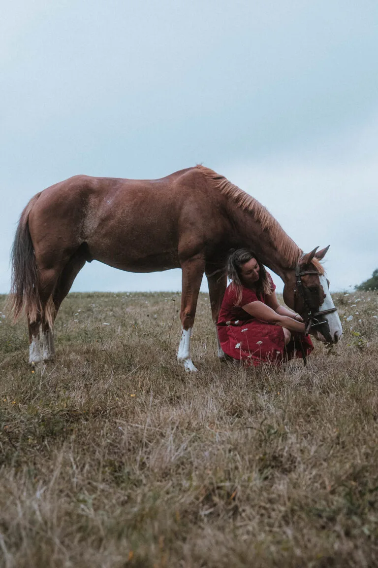 Douce scène champêtre : une femme en robe rouge près d'un cheval, instant complice lors d'un mariage dans les Landes.
