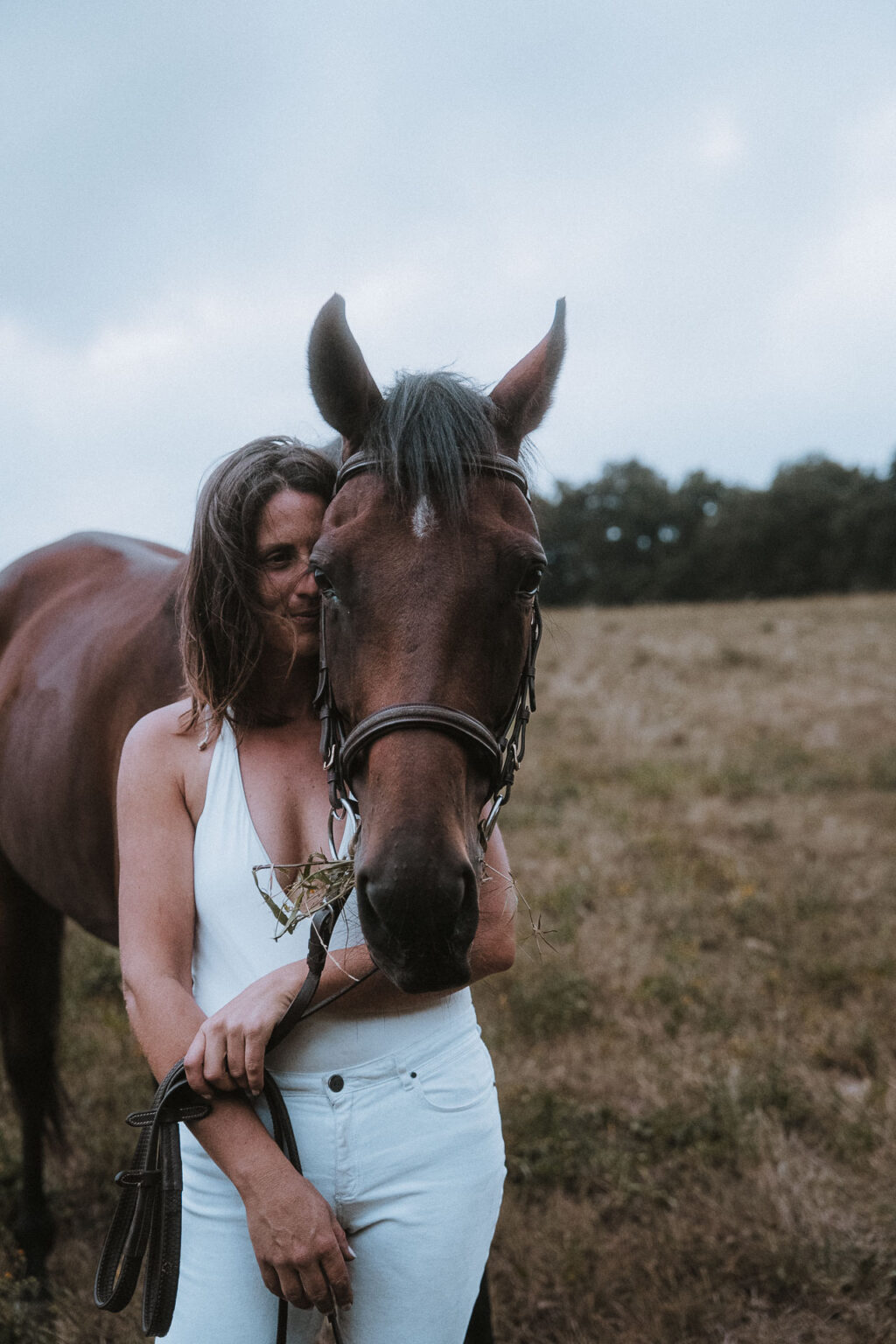 Une mariée lumineuse en prairie landaise avec son cheval, instant doux et naturel d'une fête de mariage champêtre.