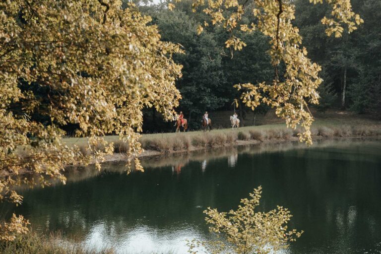 Jolie scène de mariage dans les Landes : balade à cheval près d'un étang, reflets d'arbres et ambiance paisible en famille.