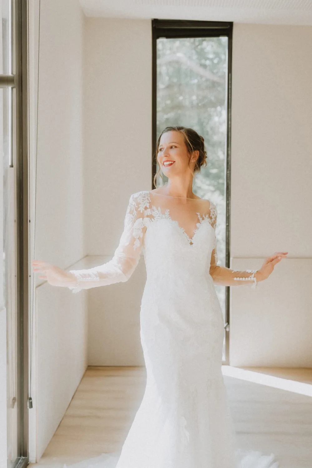 Une mariée radieuse en dentelle blanche pose près d'une fenêtre, ambiance élégante et lumineuse à Dax dans les Landes.