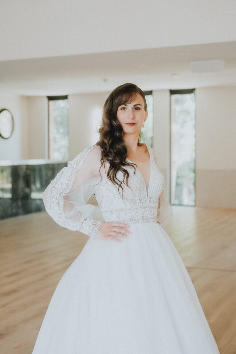 Dans une ambiance chaleureuse, une future mariée radieuse pose sur un parquet, sa robe en dentelle éclatante dans les Landes.