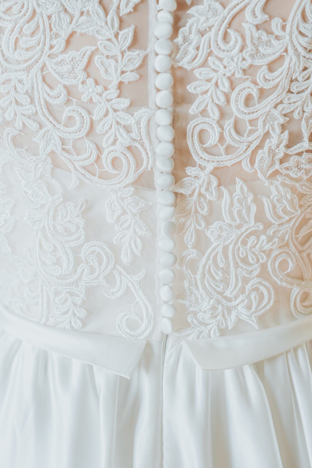 La délicatesse du dos en dentelle blanche, boutons nacrés et broderies florales pour un mariage raffiné dans les Landes.